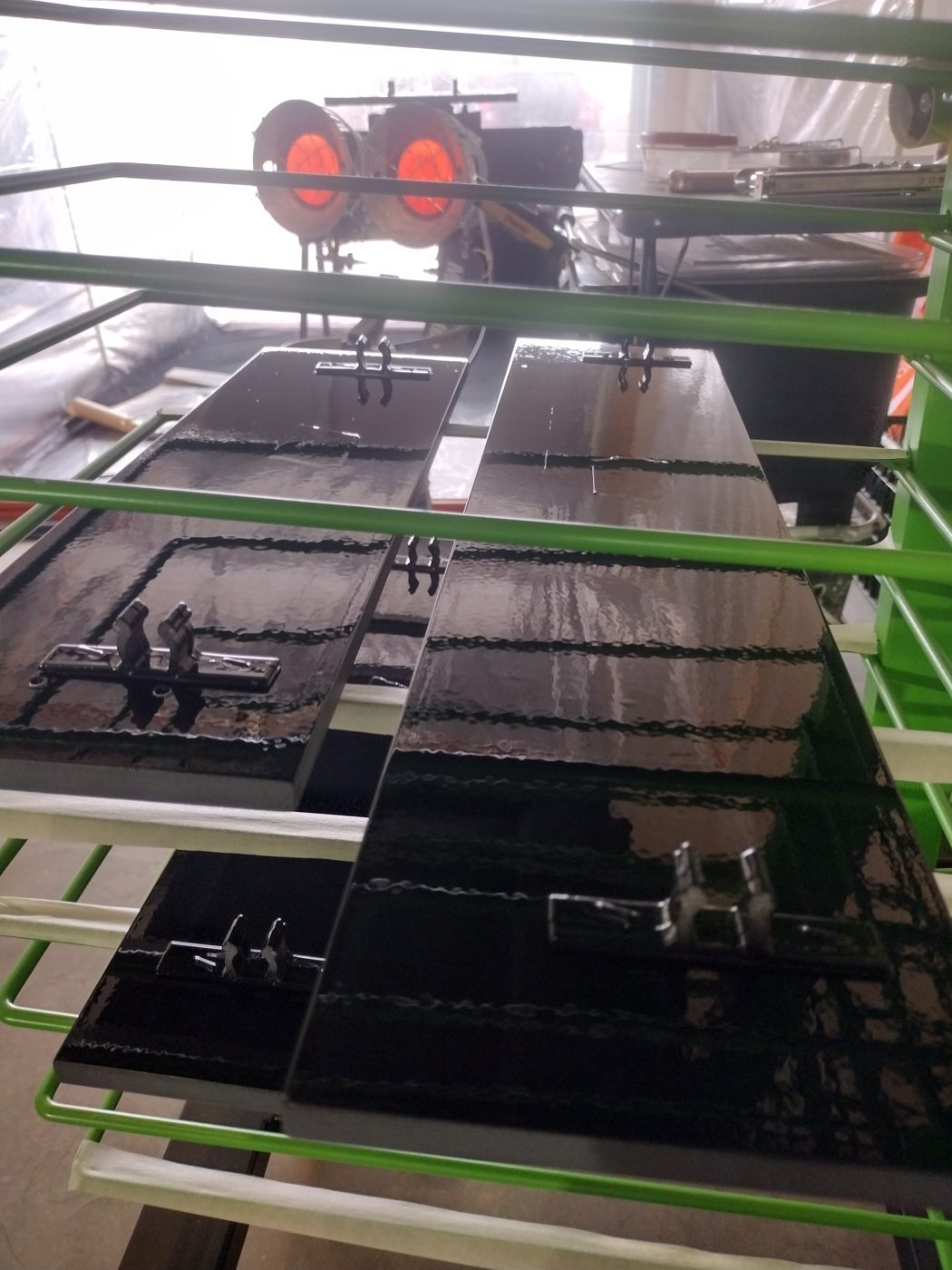 Close-up of glossy, freshly sprayed black cabinet doors drying on the rack
